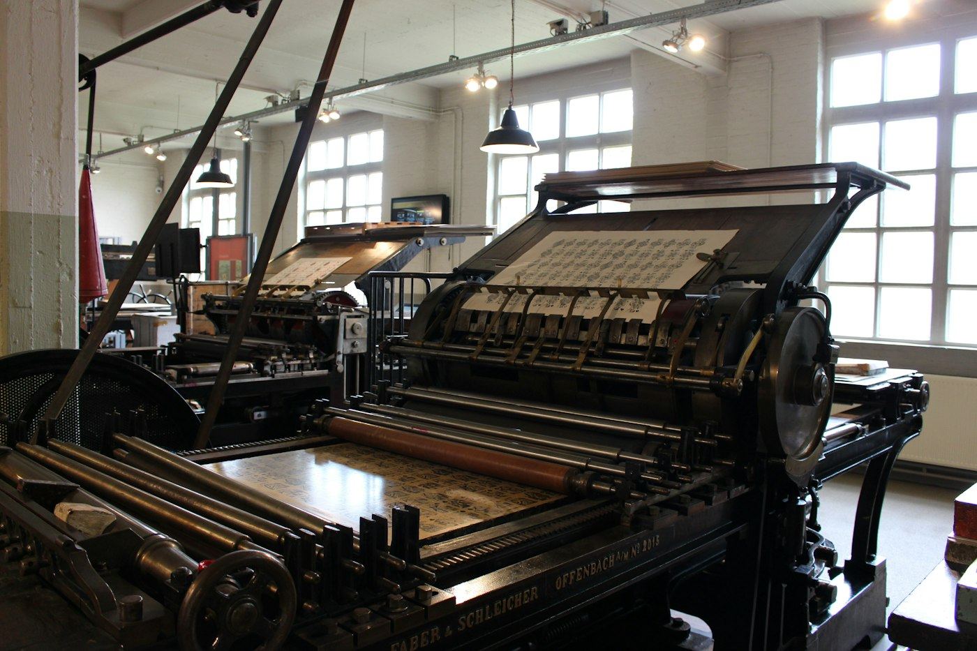 A row of older printing presses in a museum hall, with no people in the frame.