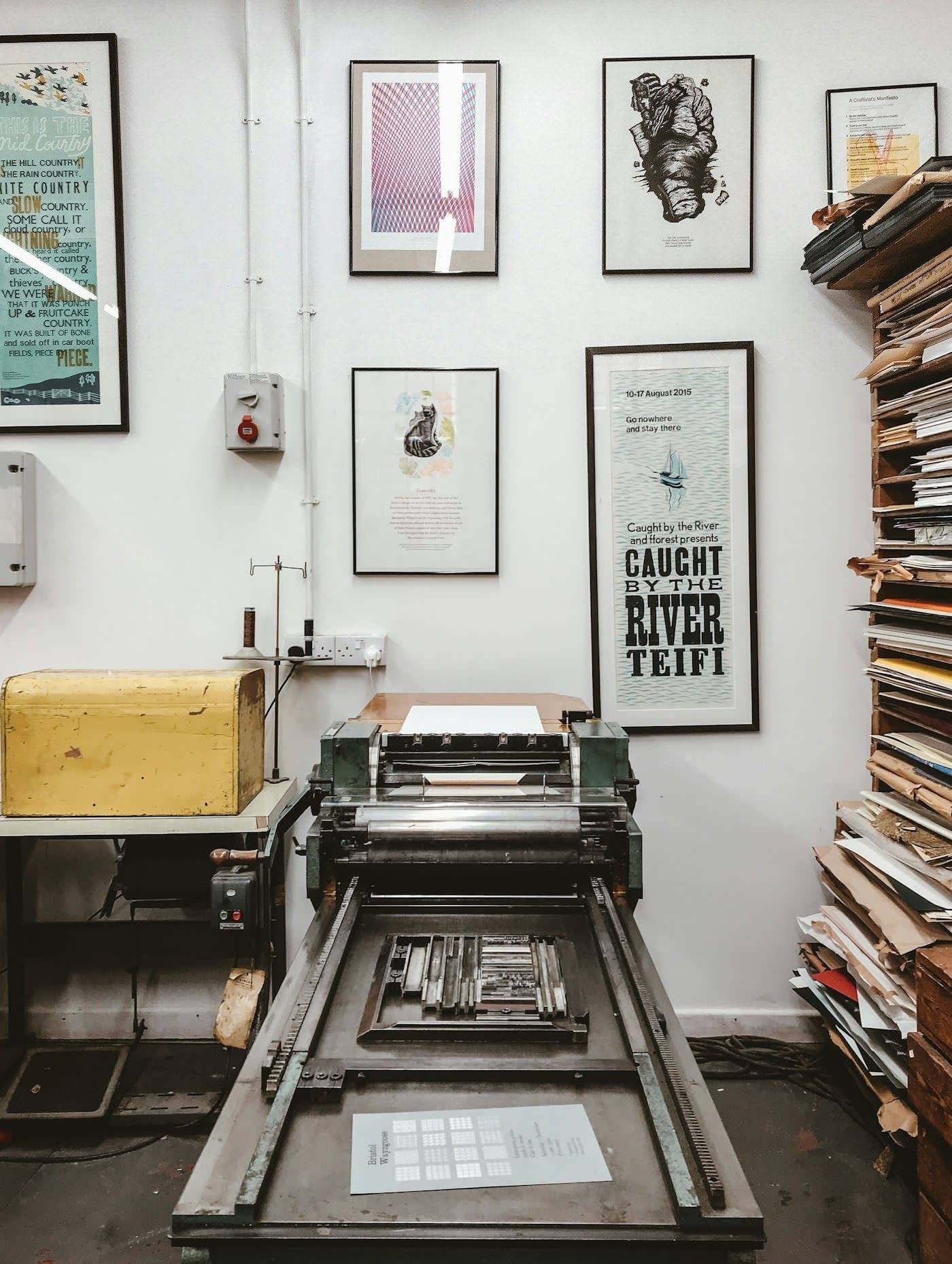 A vintage green platen printing press against a workshop wall, with no people in the frame.